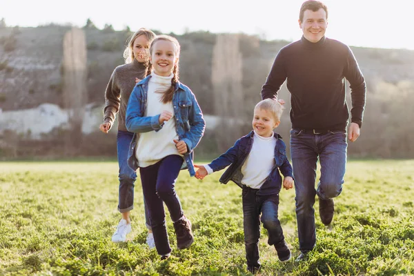 Far, mor och barn springer genom ett grönt fält. — Stockfoto