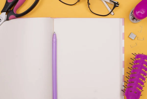 girlish pink set - glasses, notebook, pen, stapler, hairbrush on a yellow background. flatley