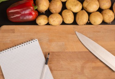 Alışveriş listesi, yemek tarifi kitabı, diyet planı. Taze çiğ sebze, meyve ve yemek pişirmek için malzemeler. üst görünüm, metin için yer. Diyet veya vegan gıda, sağlıklı pişirme kavramı. Düz yatıyordu. Reci için not defteri