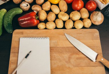 Alışveriş listesi, yemek tarifi kitabı, diyet planı. Taze çiğ sebze, meyve ve yemek pişirmek için malzemeler. üst görünüm, metin için yer. Diyet veya vegan gıda, sağlıklı pişirme kavramı. Düz yatıyordu. Reci için not defteri