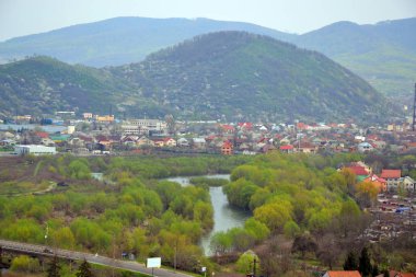 Şafakta dağların eteklerinde şehrin panoramik görünümü. Ormanlar, evler ve nehir