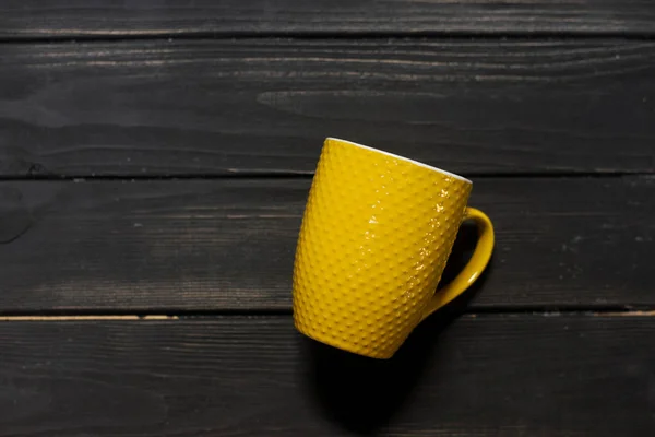 Yellow mug on a black wooden background. texture