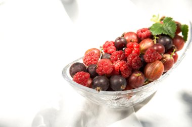 beyaz bir kumaş arka plan üzerinde şeffaf bir tabakta çilek. Gölgeler oyunu. ahududu, kuş üzümü, ahududu