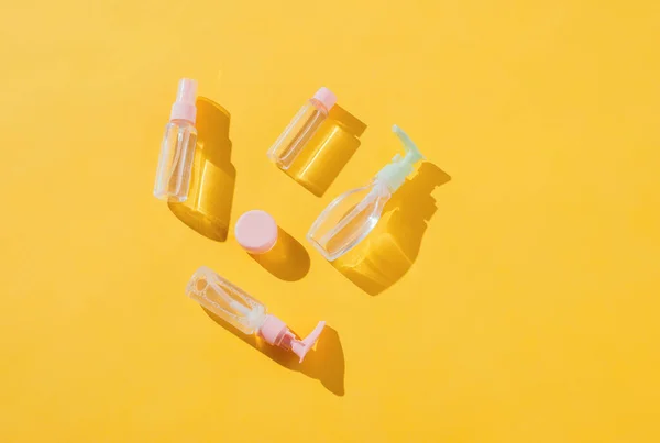 Various common beauty products in bottles - cream, soap, shampoo and perfume on a yellow background with shadows. View from above. Hard light