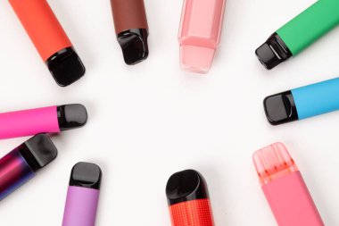 Beyaz arka planda daire şeklinde dizilmiş çeşitli renkli tek kullanımlık kalemler, modern elektronik sigara içme cihazları. Boşluğu kopyala. 