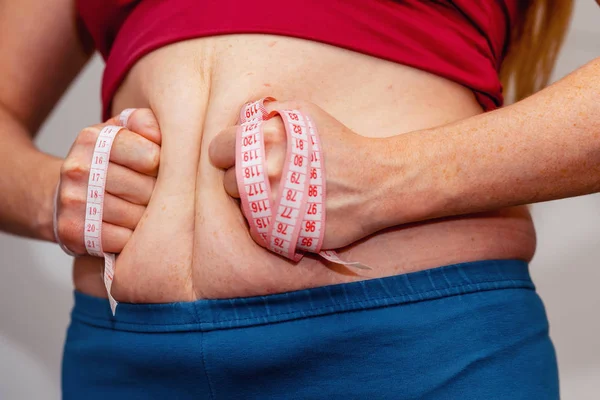 Closeup of woman pinching belly fat. Young slim woman in blue shorts pinching her abdomen. Diet and weight loss concept.