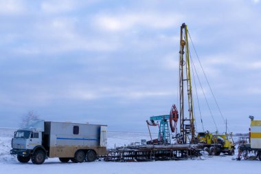 Üst sürücüden sarkan kablosuz ağ ekipmanları ağaç kesimi için aşağıya inmeye hazır. Bir petrol kuyusu mühendisi, bir petrol kuyusunun içindeki çelik kaplamanın durumunu kaydetmek için uzman bir minibüsün arkasında çalışıyor.