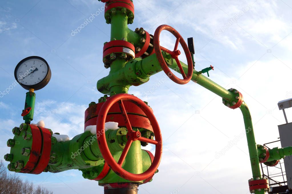 Horizontal view of a wellhead with valve armature. Oil and gas industry concept.  Oil valve with rocking in the background. Offshore oil and gas site service operator open valve for control gases.