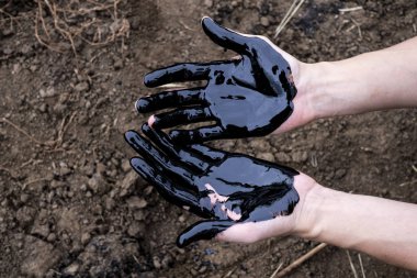 Yağ sızıntısı. Çok kirli bir el. Toprak zemininde siyah yağ olan elleri gösteriyor..