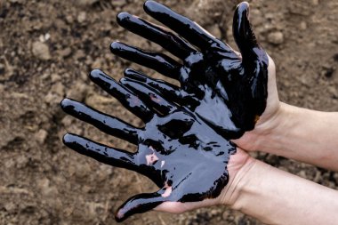Yağ sızıntısı. Çok kirli bir el. Toprak zemininde siyah yağ olan elleri gösteriyor..