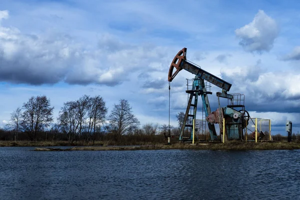 L'unità di pompaggio del fascio è compiti a casa, tramonto nel campo petrolifero. Pompa olio olio impianto di perforazione energia macchina industriale per il petrolio. L'unità di pompaggio come la pompa installata su un pozzo. Attrezzature dei giacimenti petroliferi — Foto Stock