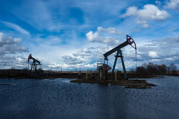 L'unità di pompaggio del fascio è compiti a casa, tramonto nel campo petrolifero. Pompa olio olio impianto di perforazione energia macchina industriale per il petrolio. L'unità di pompaggio come la pompa installata su un pozzo. Attrezzature dei giacimenti petroliferi — Foto Stock