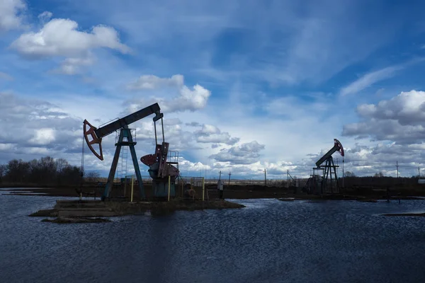 L'unità di pompaggio del fascio è compiti a casa, tramonto nel campo petrolifero. Pompa olio olio impianto di perforazione energia macchina industriale per il petrolio. L'unità di pompaggio come la pompa installata su un pozzo. Attrezzature dei giacimenti petroliferi — Foto Stock