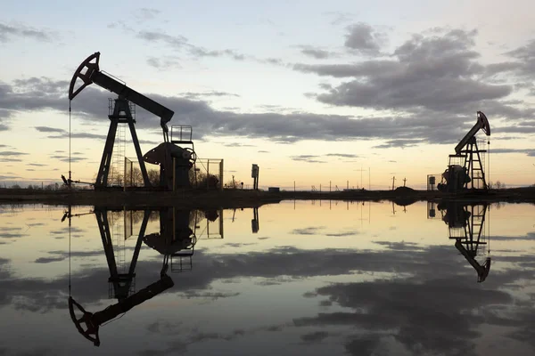 L'unità di pompaggio del fascio è compiti a casa, tramonto nel campo petrolifero. Pompa olio olio impianto di perforazione energia macchina industriale per il petrolio. L'unità di pompaggio come la pompa installata su un pozzo. Attrezzature dei giacimenti petroliferi — Foto Stock