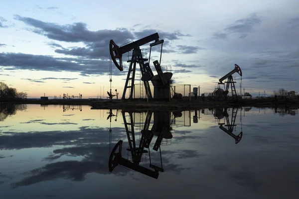 L'unità di pompaggio del fascio è compiti a casa, tramonto nel campo petrolifero. Pompa olio olio impianto di perforazione energia macchina industriale per il petrolio. L'unità di pompaggio come la pompa installata su un pozzo. Attrezzature dei giacimenti petroliferi — Foto Stock