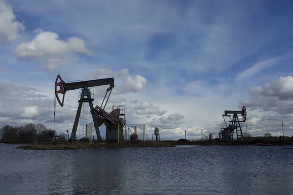 L'unità di pompaggio del fascio è compiti a casa, tramonto nel campo petrolifero. Pompa olio olio impianto di perforazione energia macchina industriale per il petrolio. L'unità di pompaggio come la pompa installata su un pozzo. Attrezzature dei giacimenti petroliferi — Foto Stock