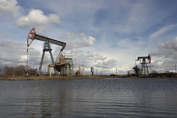 L'unità di pompaggio del fascio è compiti a casa, tramonto nel campo petrolifero. Pompa olio olio impianto di perforazione energia macchina industriale per il petrolio. L'unità di pompaggio come la pompa installata su un pozzo. Attrezzature dei giacimenti petroliferi — Foto Stock