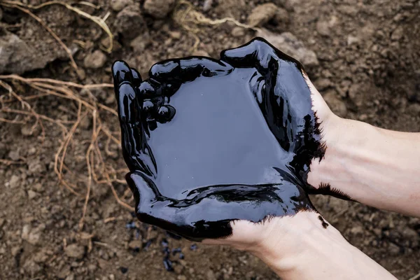 Olajszivárgás. Nagyon piszkos kez.Foltos kéz mutatja hüvelykujját fel fekete olaj a talaj hátterében. — Stock Fotó