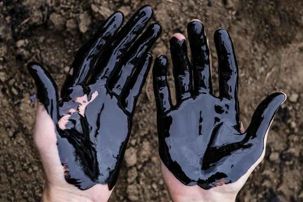 Olajszivárgás. Nagyon piszkos kez.Foltos kéz mutatja hüvelykujját fel fekete olaj a talaj hátterében. — Stock Fotó