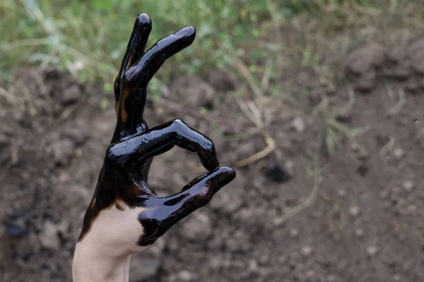 Öl ausgelaufen. sehr schmutzige Hand.Flecken Hände zeigen Daumen nach oben mit schwarzem Öl auf dem Boden Hintergrund. Hand zeigt ok — Stockfoto