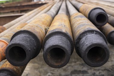 Sondaj borusu. Paslı matkap boruları kuyu bölümünde delindi. Çukur delme kulesi. Petrol ve gaz deposunun açık avlusuna döşenmiş matkap boruları ve boruların kabuğunun görünümü.