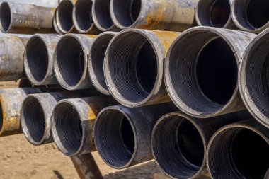 Sondaj borusu. Paslı matkap boruları kuyu bölümünde delindi. Çukur delme kulesi. Petrol ve gaz deposunun açık avlusuna döşenmiş matkap boruları ve boruların kabuğunun görünümü.
