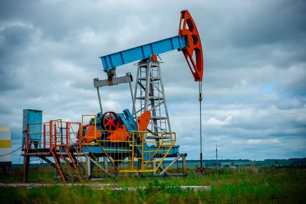 Oil field with pump jack, profiled on blue sky with white clouds, on a sunny day in spring