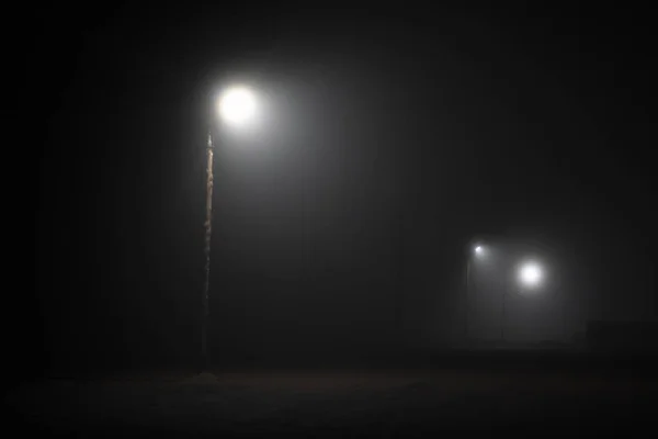 Gatubelysningen dimmigt dimmiga nattlampa post lanternor öde väg. Lonely Street på natten i ljuset av lyktor. dimmigt natt parkeringsplats — Stockfoto