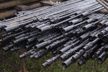 Yağ Matkap borusu. Paslı matkap boruları kuyu bölümünde delindi. Çukur delme kulesi. Boruyu güverteye döşeyin. Avluya döşenmiş matkap borularının kabuğunun görünümü. pompa çubuğu