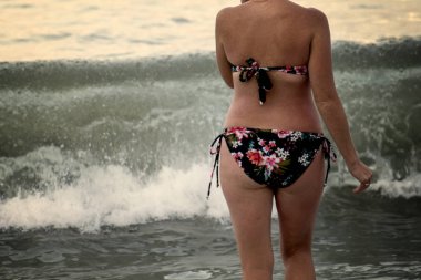 Kadın kalçaları yağ ile kaplıdır. Selülit. Mayo giyen kadın plajda kumda yürüyor. Mayo giymiş şişman kadın.