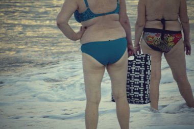 Kadın kalçaları yağ ile kaplıdır. Selülit. Mayo giyen kadın plajda kumda yürüyor. Mayo giymiş şişman kadın.