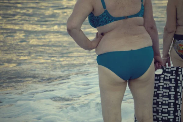 Female buttocks is covered with fat. Cellulite. Woman in swimsuit walks in the sand at the beach. Big fat female in swimsuit. — Stock Photo, Image