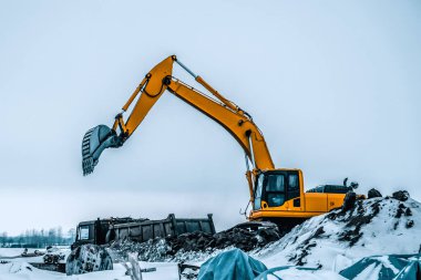 Kazı makinesi kazıları kamyona yüklüyor. Kazı makineleri ağır inşaat ekipmanlarıdır. Dönen platformda bir boom, dipper veya stick, kova ve taksiden oluşur..
