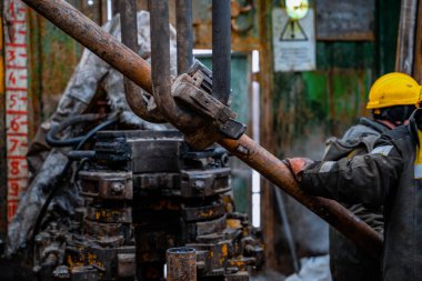 Üniformalı, kask ve gözlüklü iki matkap, sondaj kuyusundan çıkardıktan sonra sondaj borularını yerleştiriyor. Çalışan insan kavramı