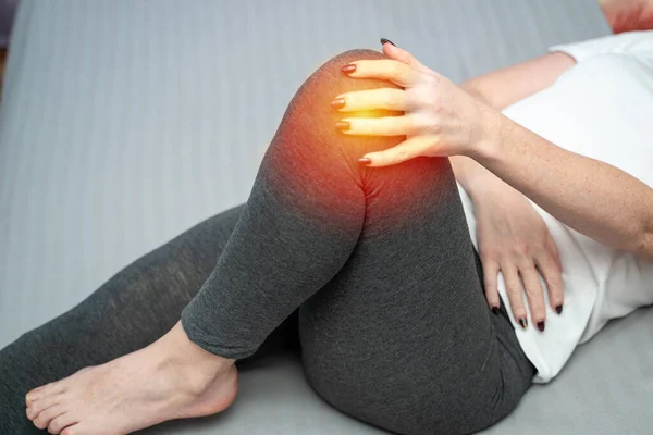 Dizi ağrıyan çekici bir kadın. Dairede yatakta oturuyor. Kadın bacağındaki tendon eklem sorunları kırmızı noktayla belirtilmiş.