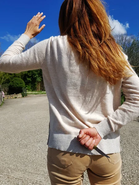 Girl back view. The hand behind the back. Knife in hand. On the background of nature.