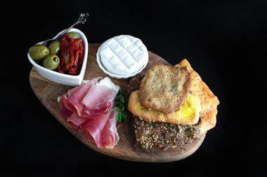  Çıtır pizza, prosciutto, yumuşak peynir, yeşil zeytin, ahşap tabakta kurutulmuş domates. Siyah arka planda izole edilmiş. Natürmort