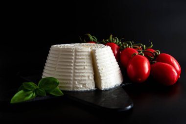 Siyah plaka üzerinde fesleğen ve kiraz domates ile taze ricotta peyniri, siyah arka plan, yan görünüm üzerinde izole. İtalyan yemek konsepti. Natürmort.