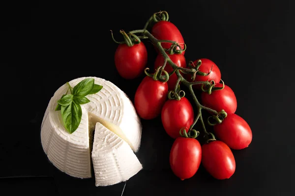 Ricotta fresca con basilico e pomodorini su piatto nero, isolata su fondo nero, vista dall'alto. Concetto di cibo italiano. Natura morta . — Foto Stock