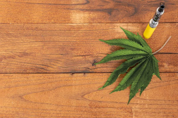 Marijuana/cannabis Leaf med elektronisk cigarett på trä bakgrund, kopiera utrymme. Flat Lay — Stockfoto