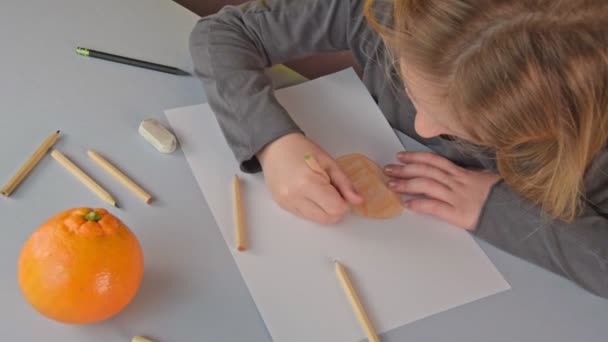Милая маленькая блондинка рисует спелый оранжевый с цветными карандашами — стоковое видео