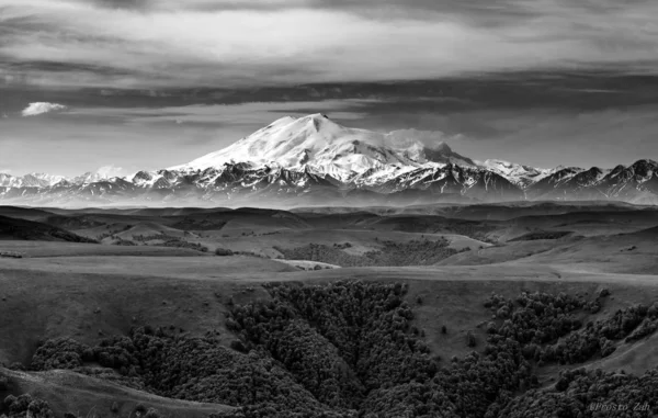 Black and white photograph of hills and valleys on the background of snow-covered Mount Elbrus