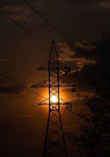 Steel mast of high-voltage wires with a lattice structure on the background of the sky filled with rays of the setting sun