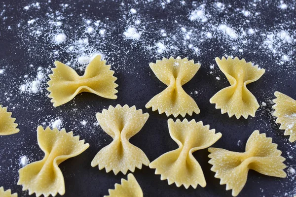 Appetizing pasta with your own hands - elegant bows on a dark background, sprinkled with light wheat flour close-up