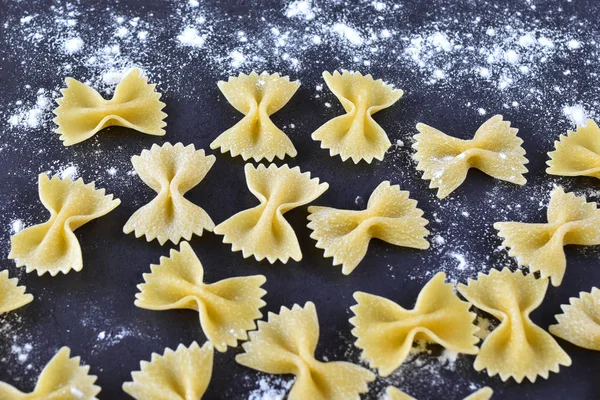 Appetizing pasta with your own hands - elegant bows on a dark background, sprinkled with wheat flour close-up