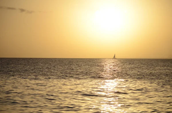 Gently yellow sunset light over the sea with a lone distant sail on the horizon