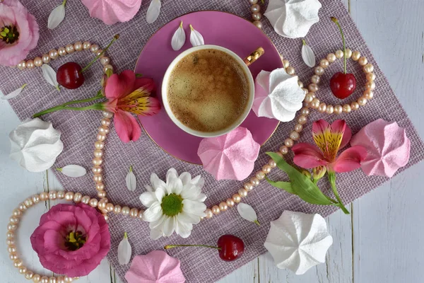 Flat lay with a pink cup of coffee with delicious foam, flowers, sweets and pearls close-up