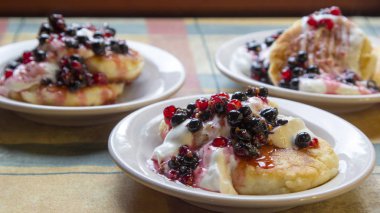 Ev yapımı cheesecakes ekşi krema ve kırmızı ve siyah frenk üzümü sos ile.