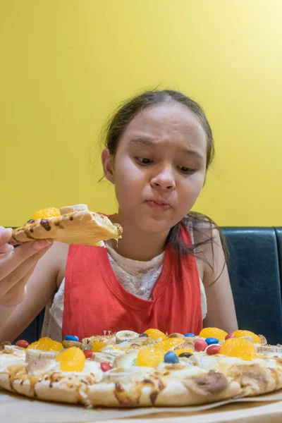 Young mixed race tween girl eating bad tasting candy, marshmallow, and chocolate pizza
