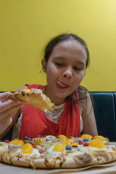 Young mixed race tween girl eating candy, marshmallow, and chocolate pizza, licking lips
